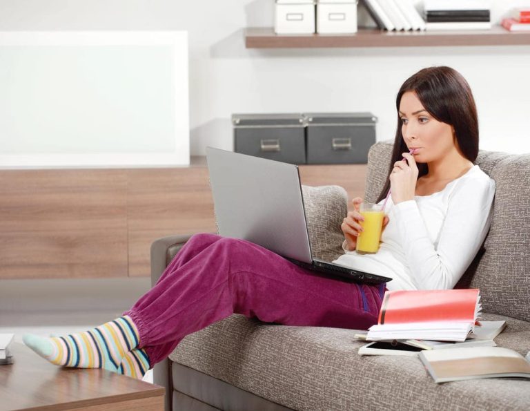 Woman sipping juice while working on a laptop at home