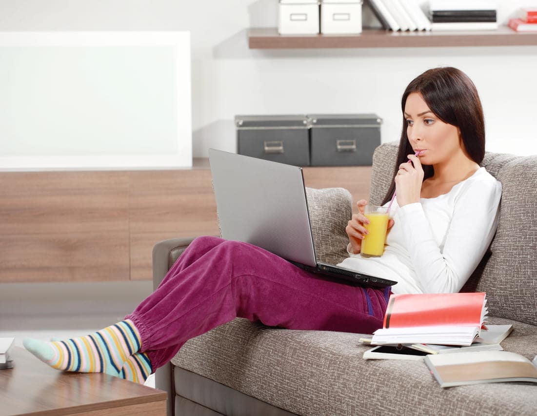 Woman sipping juice while working on a laptop at home