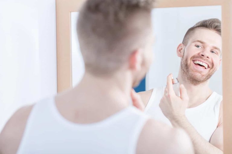 Man applying cologne while smiling at the mirror