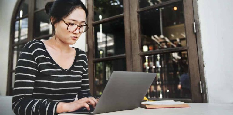 Woman wearing glasses working on a laptop at a café