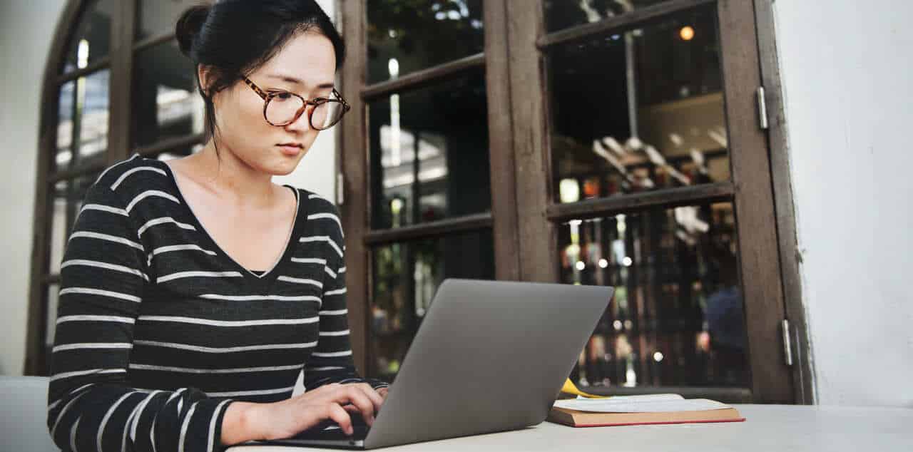 Woman wearing glasses working on a laptop at a café
