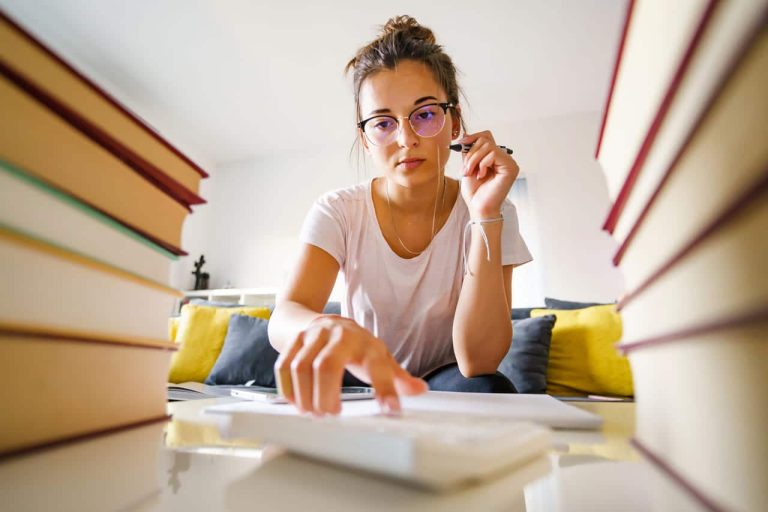 A woman studying, surrounded by books, using a calculator