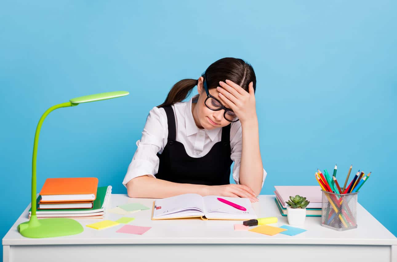 Girl in glasses looking frustrated while studying at her desk