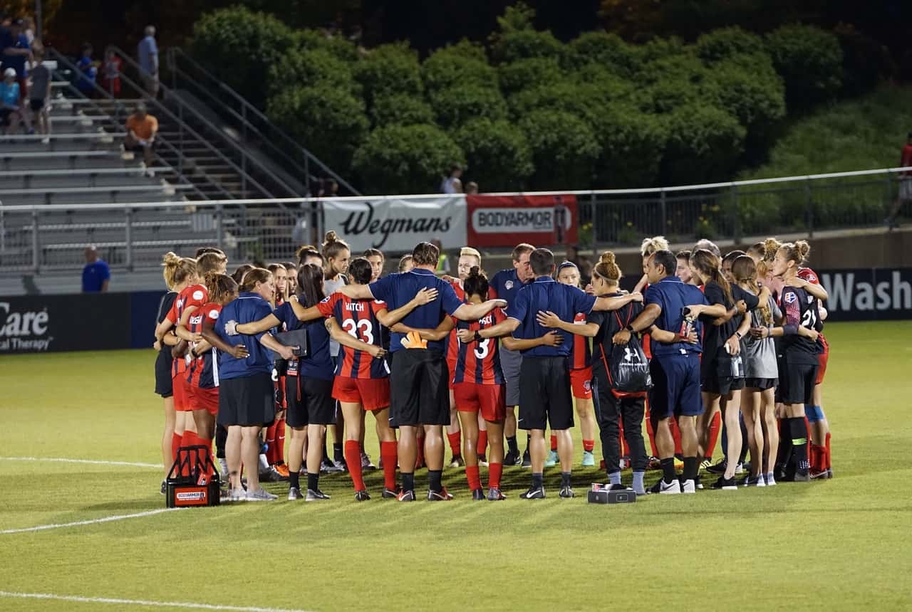A women’s soccer team huddles together on the field before or after a match