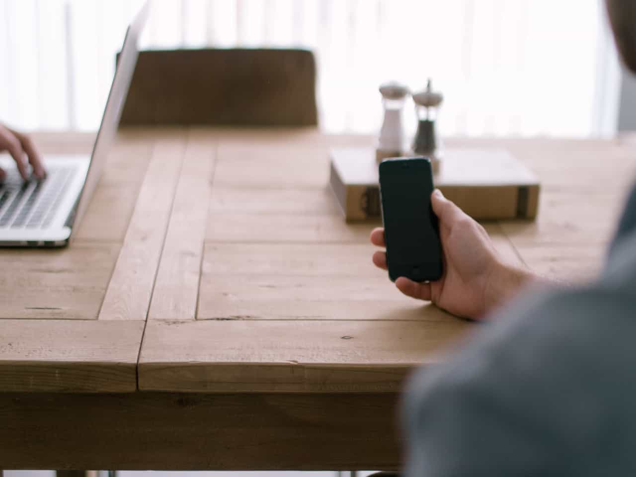 Person holding a phone while another works on laptop