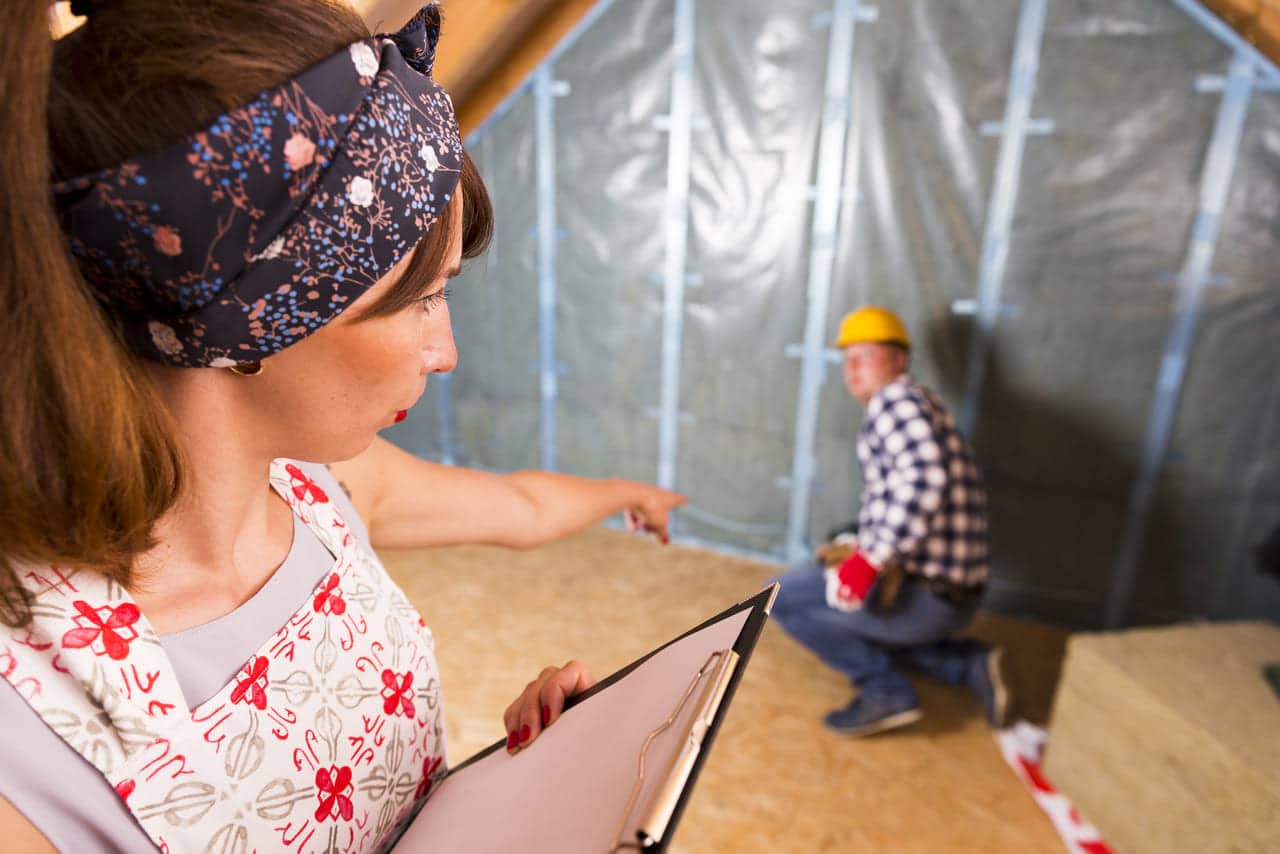 Woman with clipboard supervising construction worker in an attic