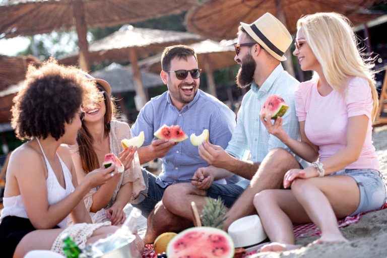 A group of friends enjoying watermelon at a beach picnic