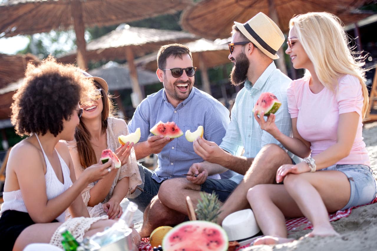 A group of friends enjoying watermelon at a beach picnic