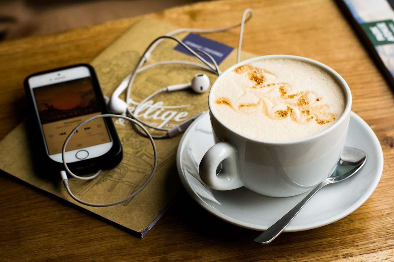 A cup of coffee beside a phone with earphones