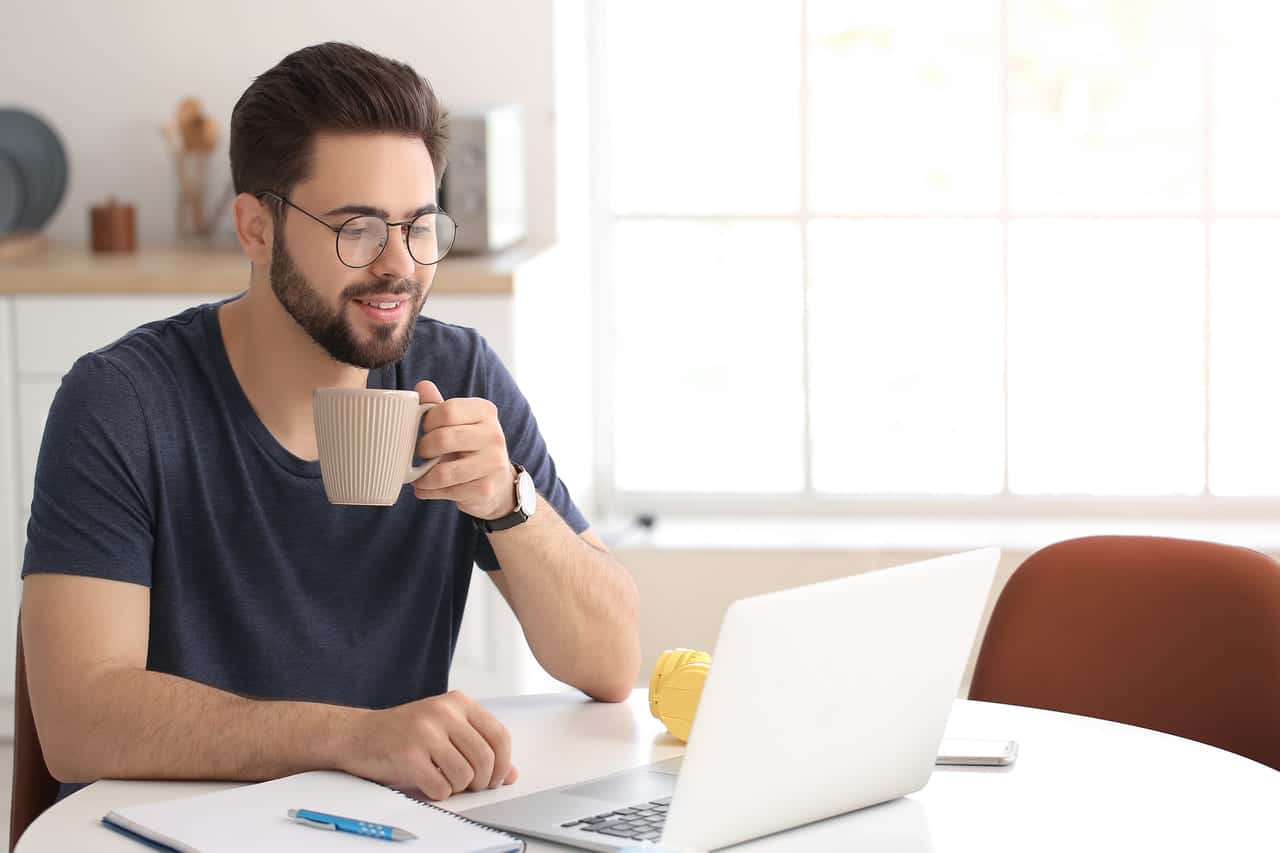 A man drinking coffee while working on a laptop