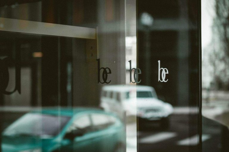 Glass window reflecting street scene with the word "be"