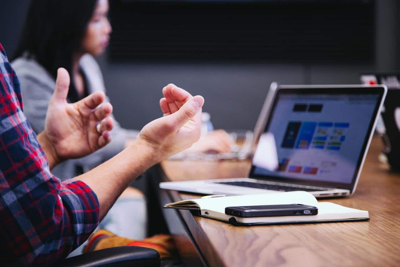 Person gesturing while working on a laptop at meeting
