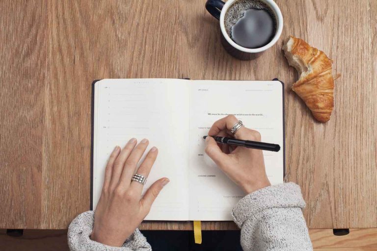 Handwriting in a notebook with coffee and croissant nearby
