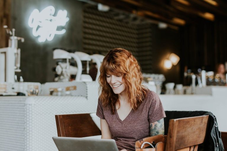 Woman smiling while using a laptop in a café