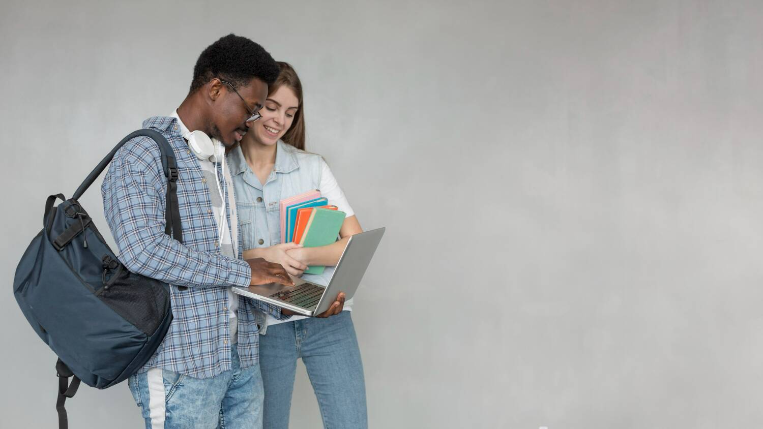 Two students looking at a laptop while holding books and backpacks.