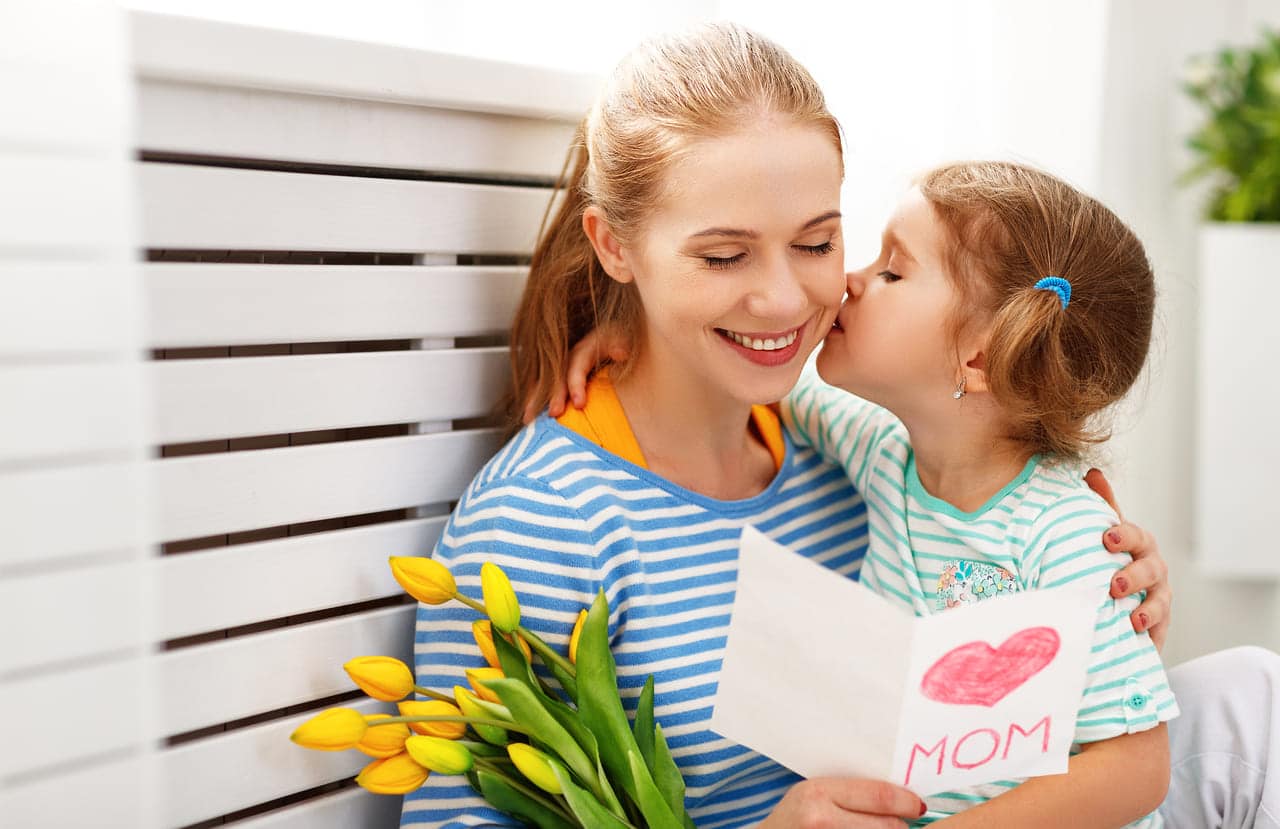 Child kissing mother holding flowers and card