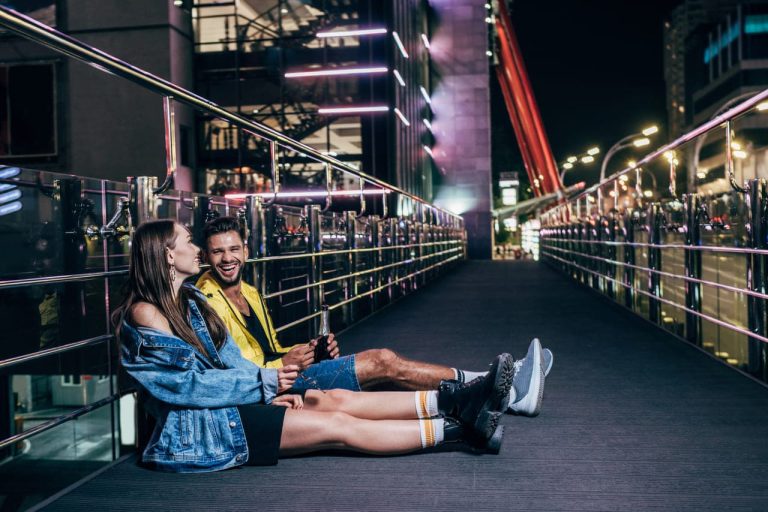 Couple sitting on a bridge at night, smiling
