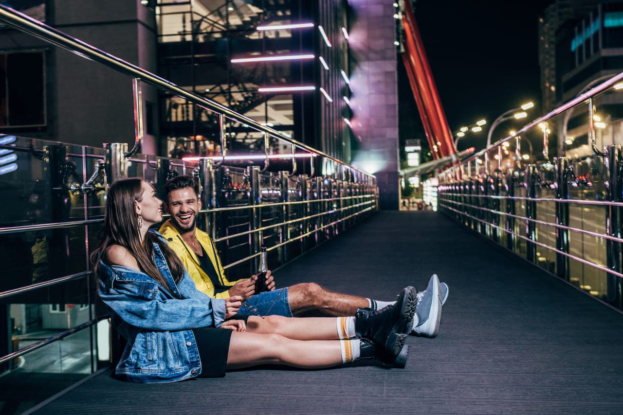 Couple sitting on a bridge at night, smiling
