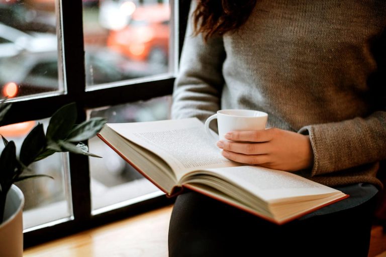 Person reading a book while holding a cup of coffee