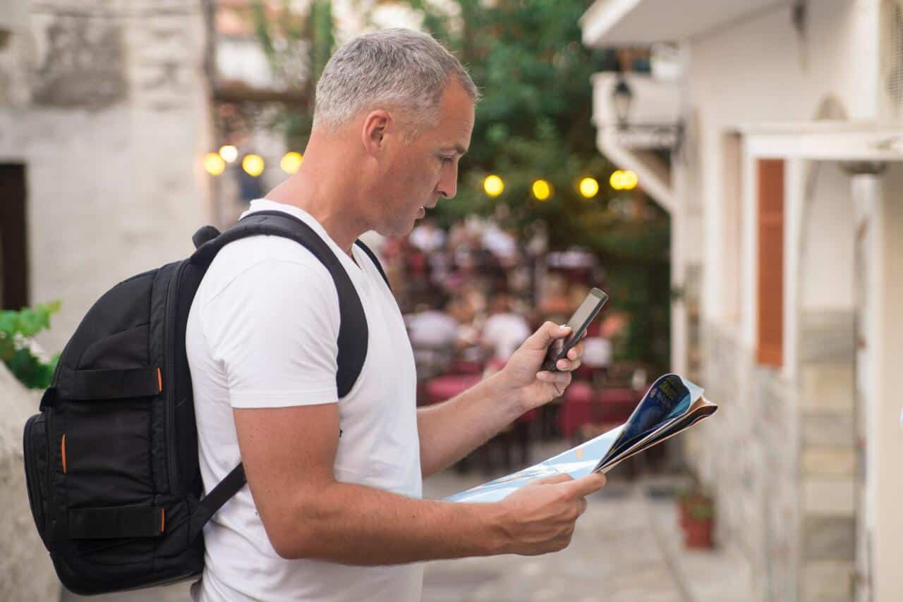 A man with a backpack looking at his phone while holding a map