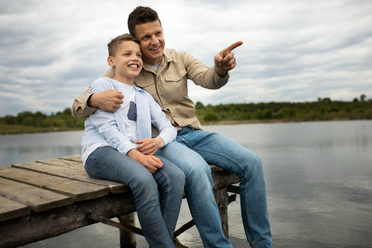 Father and son sitting on dock by lake