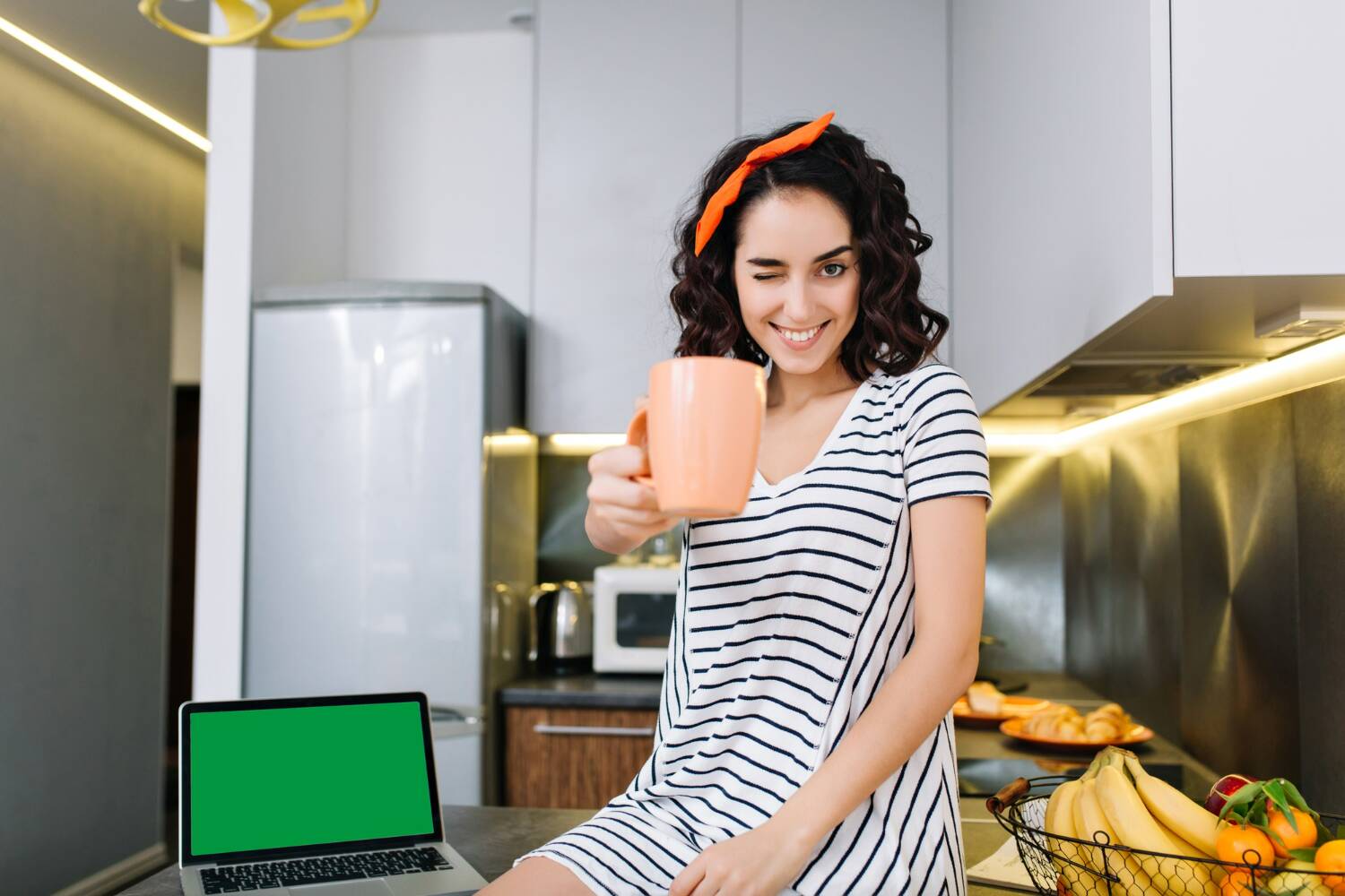 Person winking while holding a mug in the kitchen