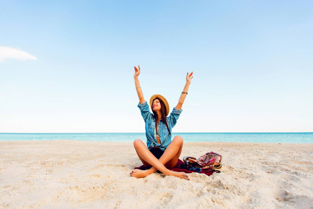 Person sitting on beach, arms raised in joy