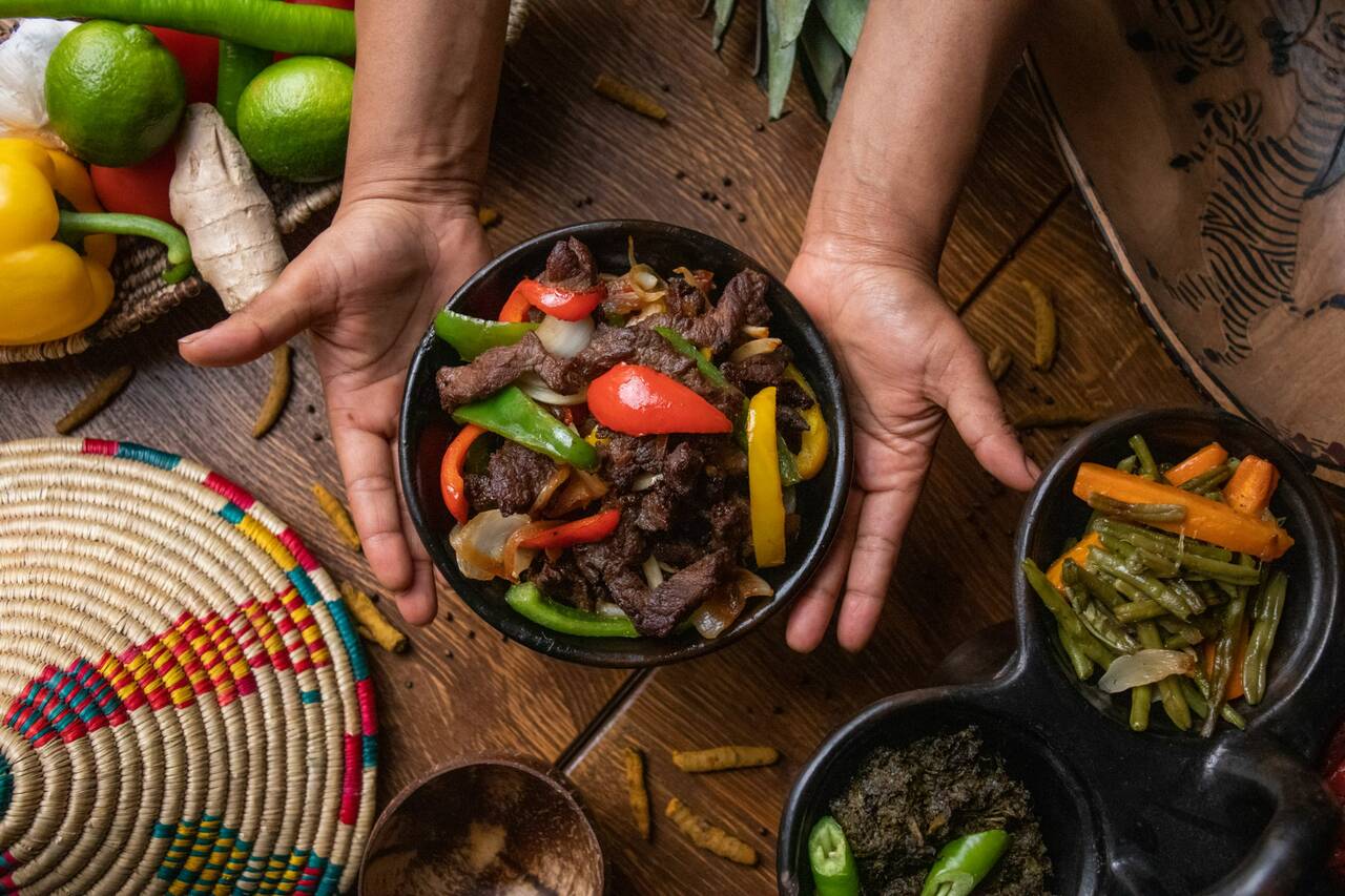 Hands holding a bowl of stir-fried beef and vegetables