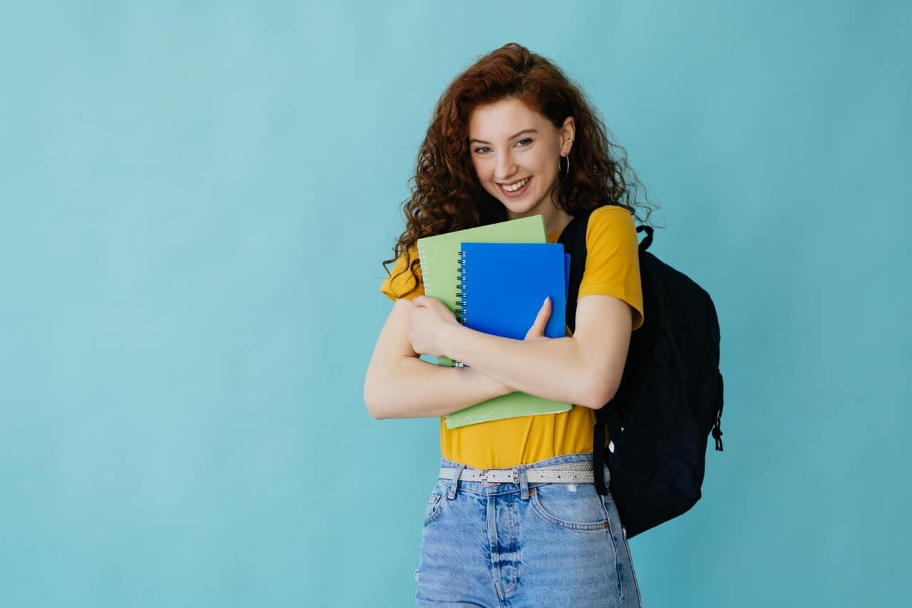 Student smiling while holding books and wearing a backpack