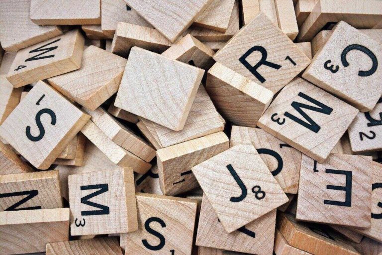 A pile of wooden Scrabble tiles with black letters and point values.