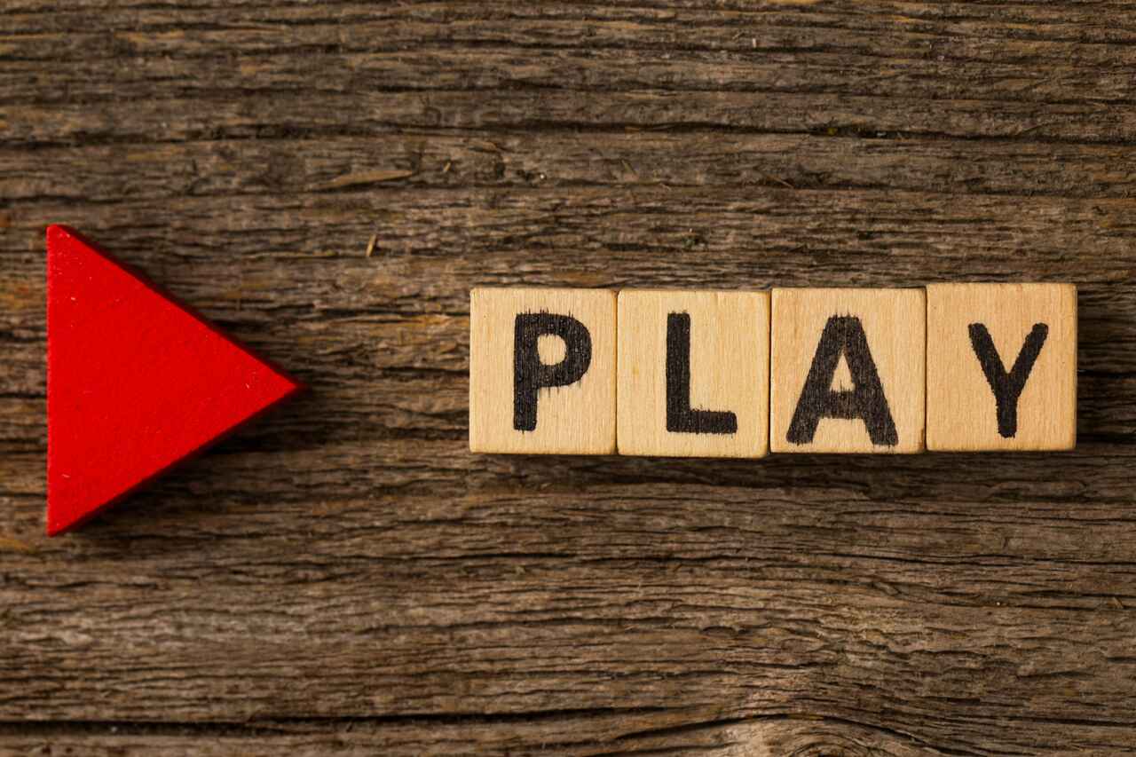 Wooden blocks spelling “PLAY” with a red triangle on the left.