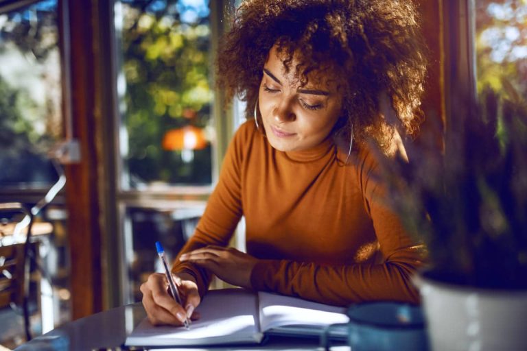 Woman in an orange sweater writing in a notebook at a café