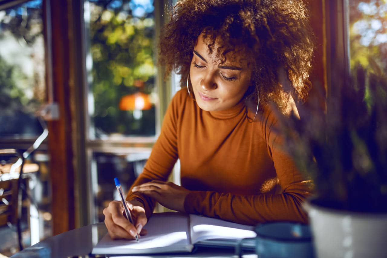 Woman in an orange sweater writing in a notebook at a café