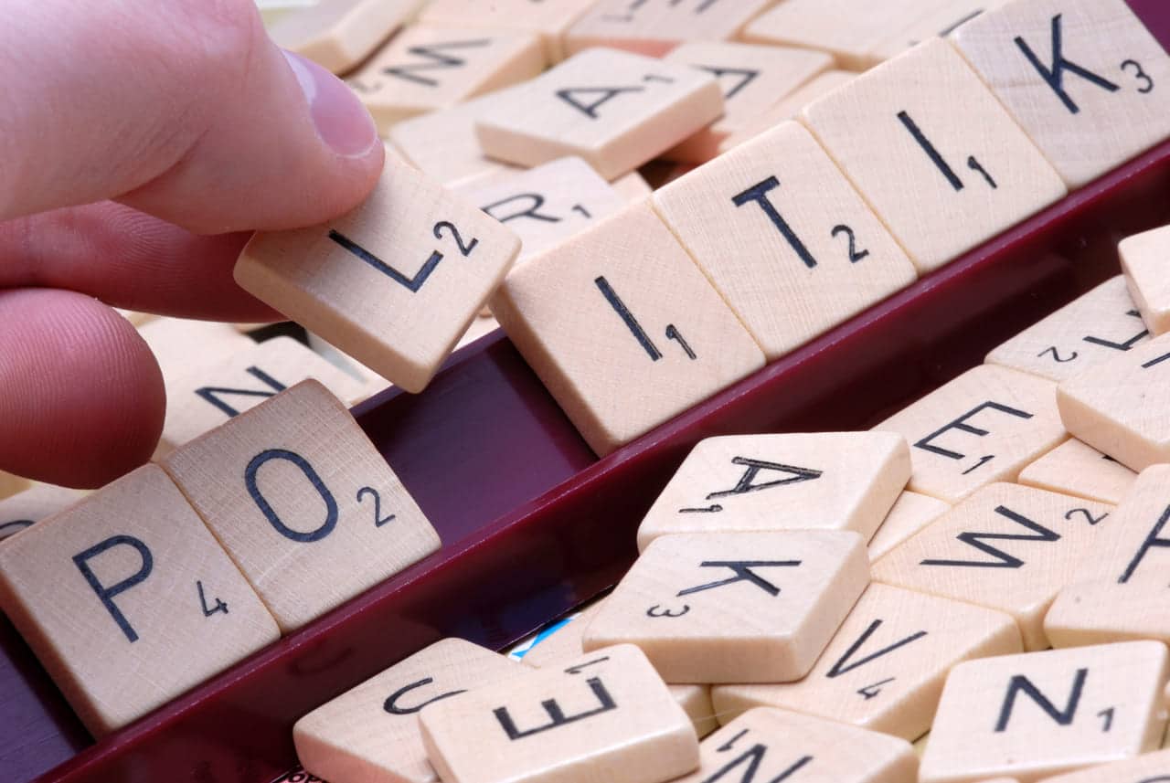 Hand placing Scrabble tiles to spell "POLITIK" on a game board