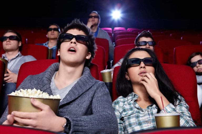 People in a theater wearing 3D glasses, eating popcorn.