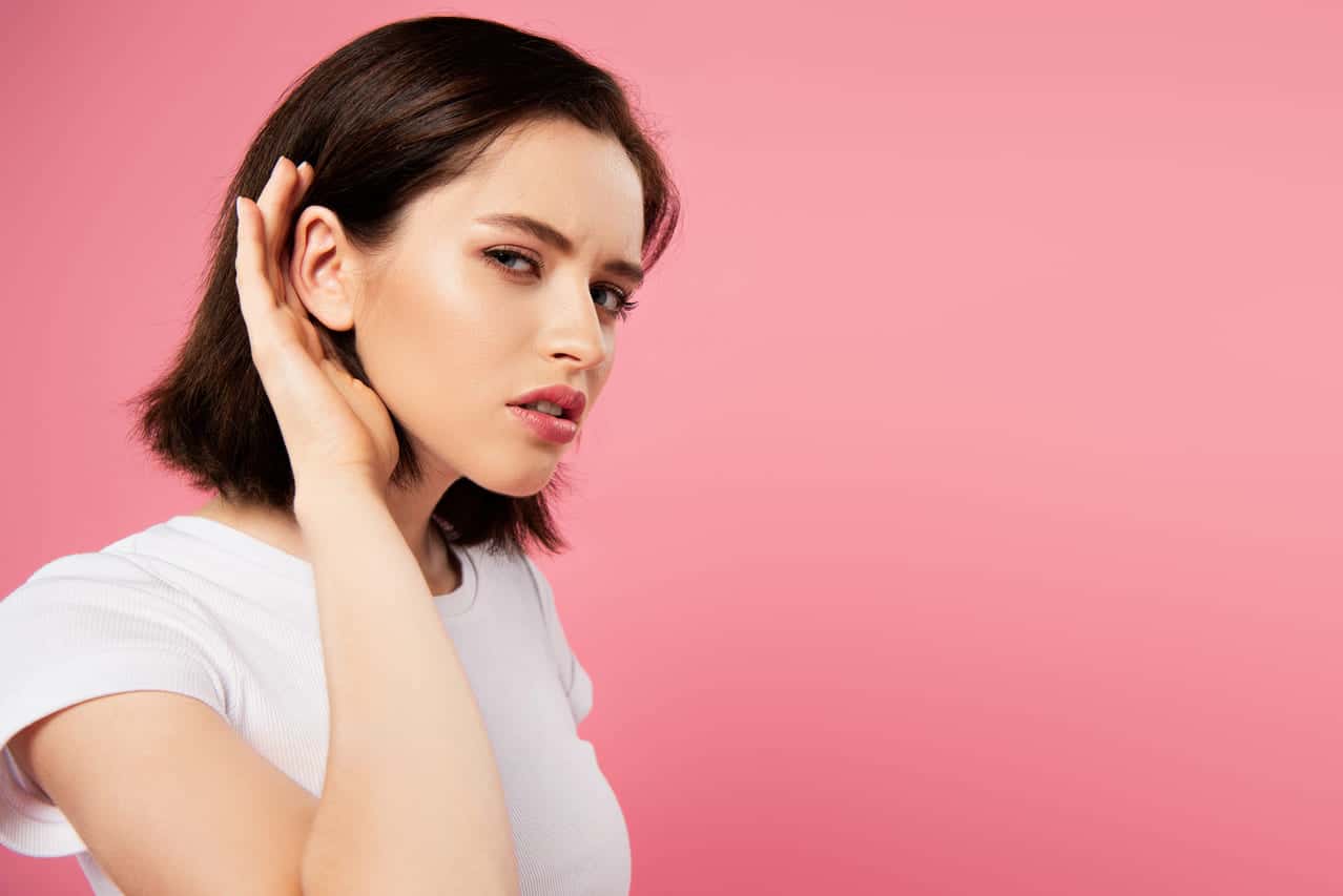 Woman leaning forward with hand to ear, listening intently