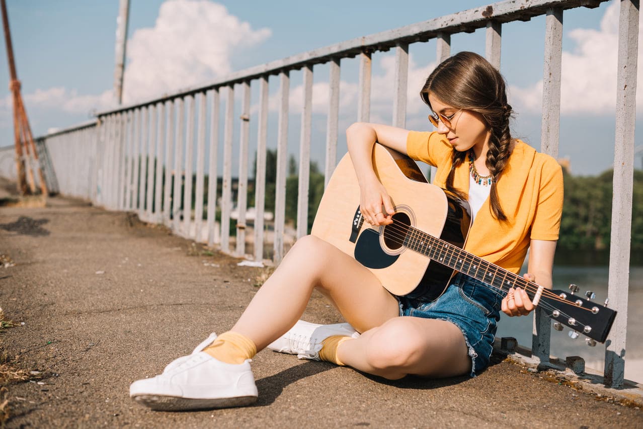 A woman sitting by a railing, playing an acoustic guitar