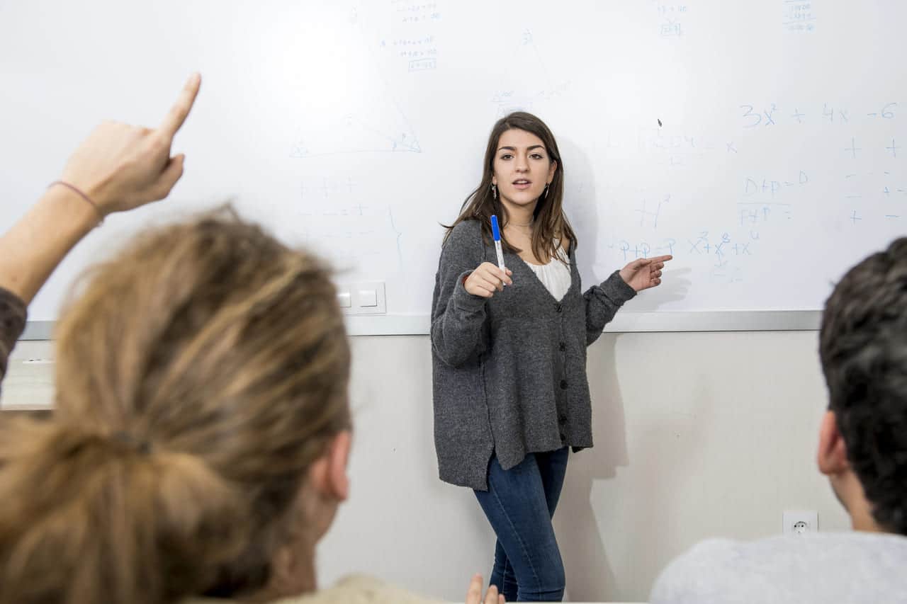A teacher explains a concept at a whiteboard to students.