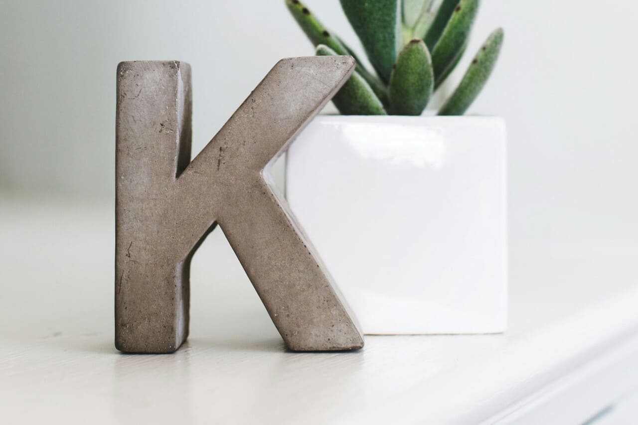 Concrete "K" next to a white potted plant.