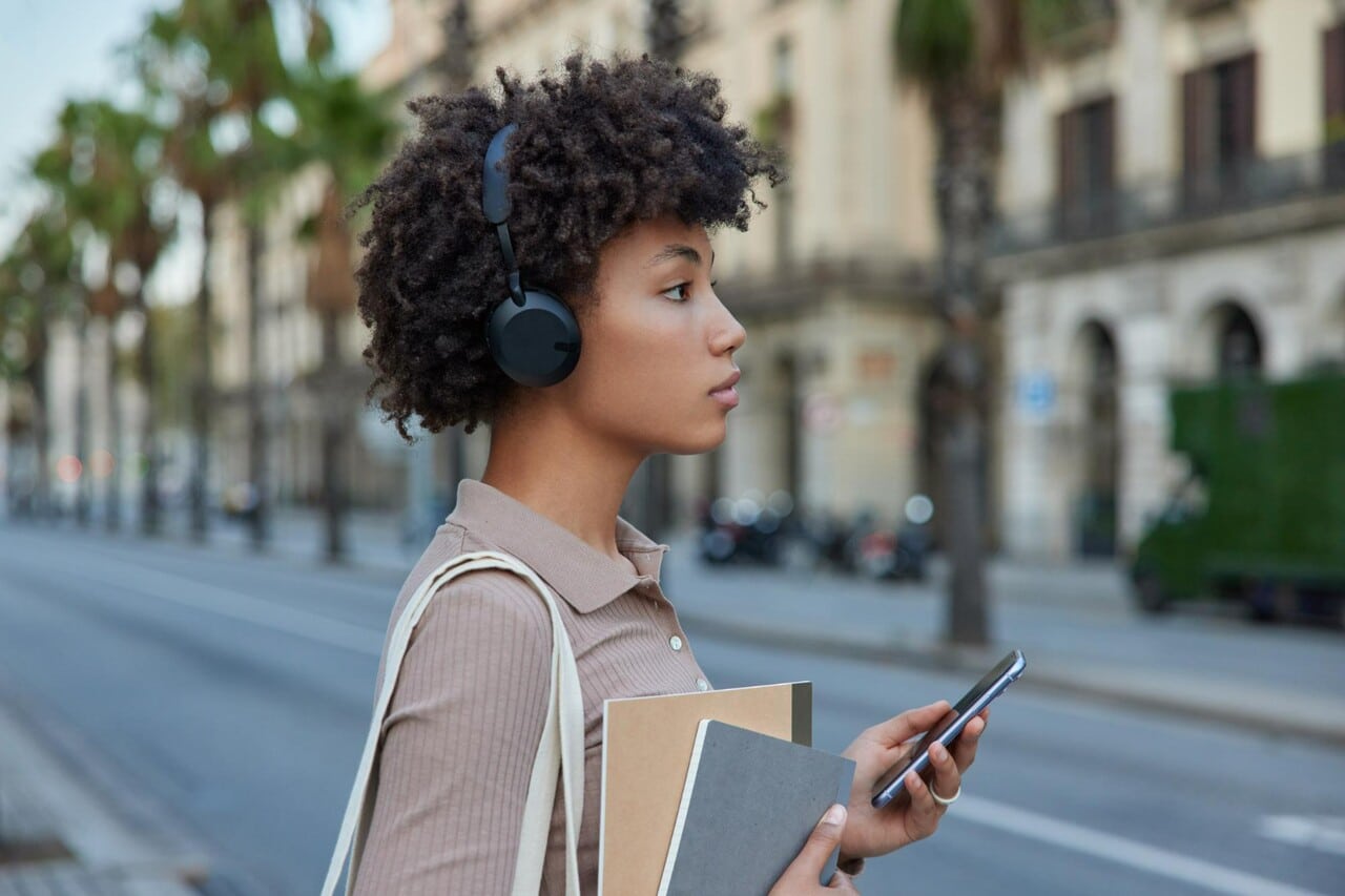 Woman with headphones holding books and using phone