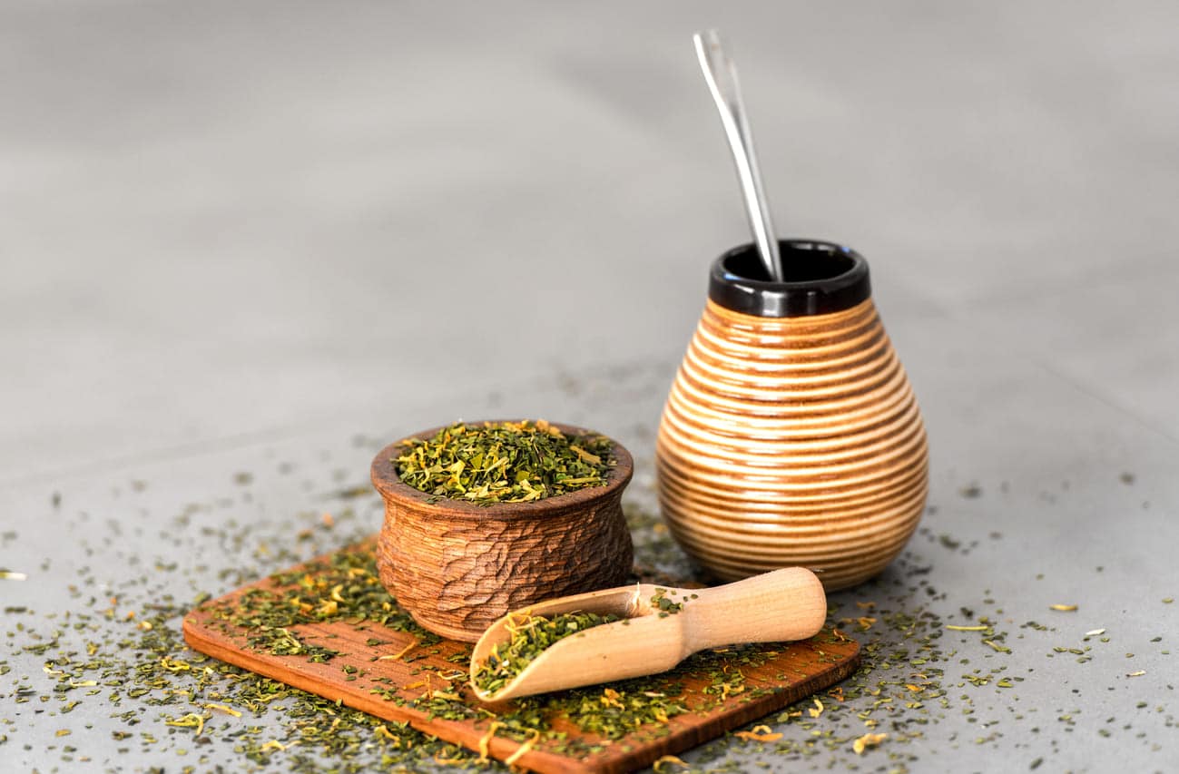 Yerba mate tea leaves in wooden bowl with traditional mate cup