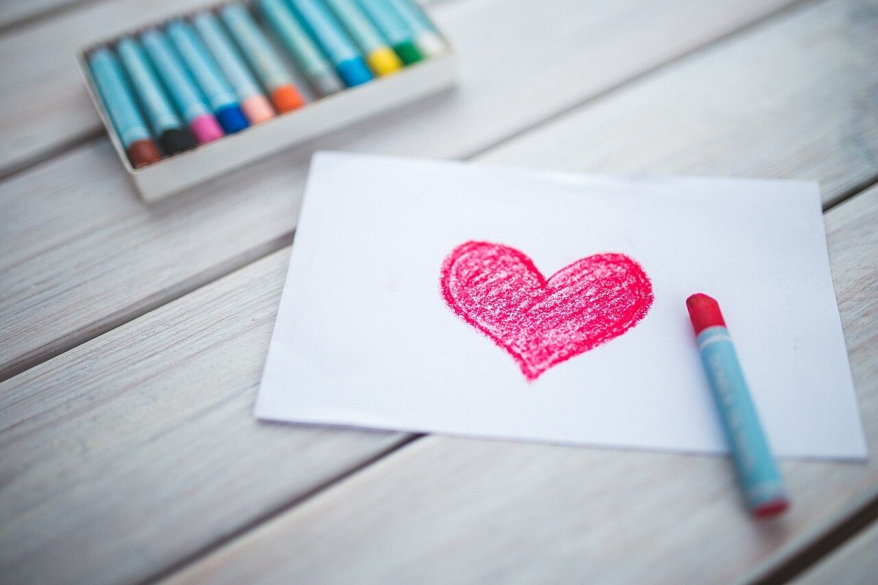 Crayon heart drawing on paper with crayons nearby