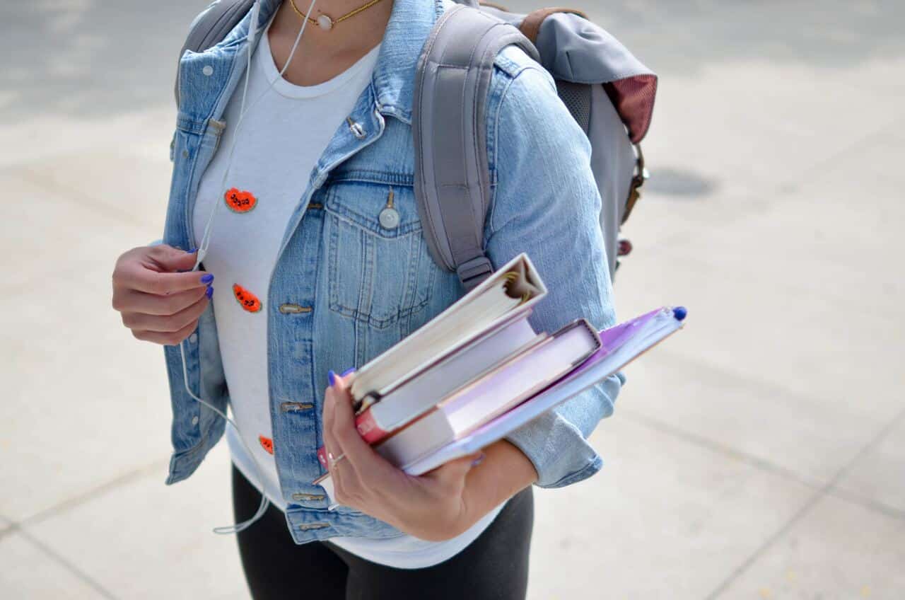 Person holding books and wearing a backpack