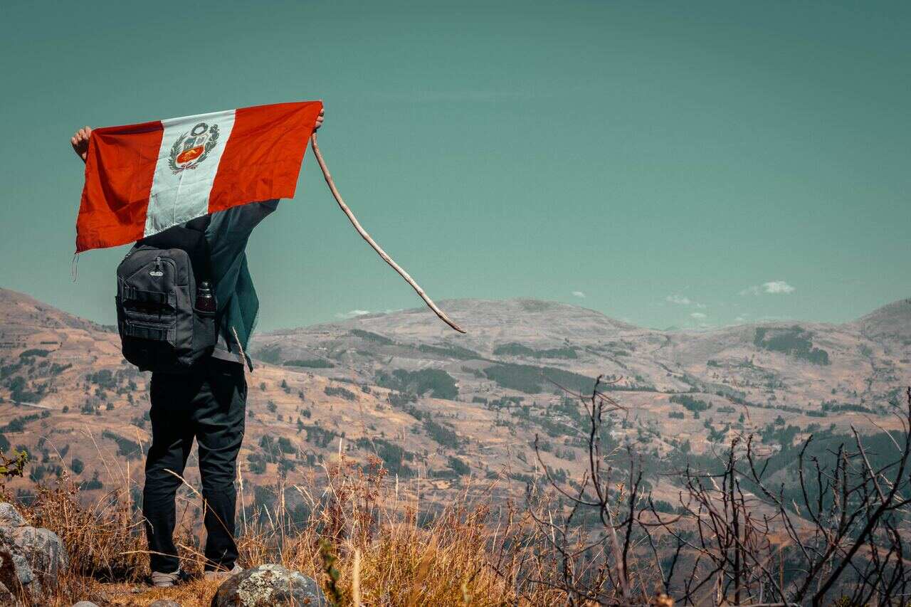 Hiker holding the Peruvian flag over scenic mountains