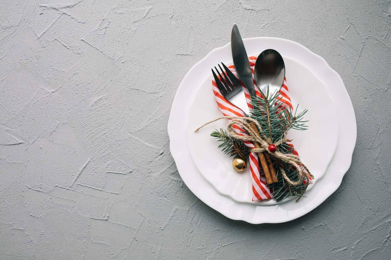 Christmas-themed plate setting with cutlery wrapped in festive decor
