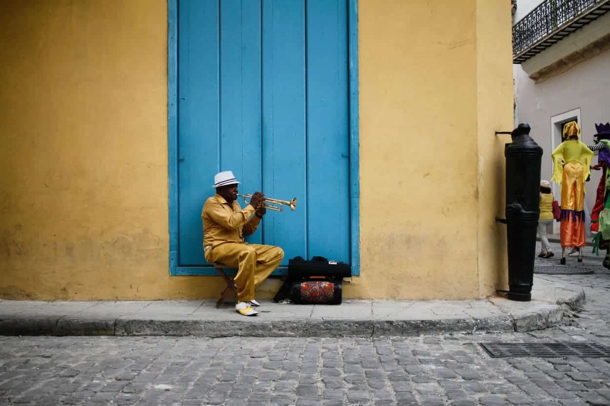 Street musician playing trumpet near a blue door in Cuba