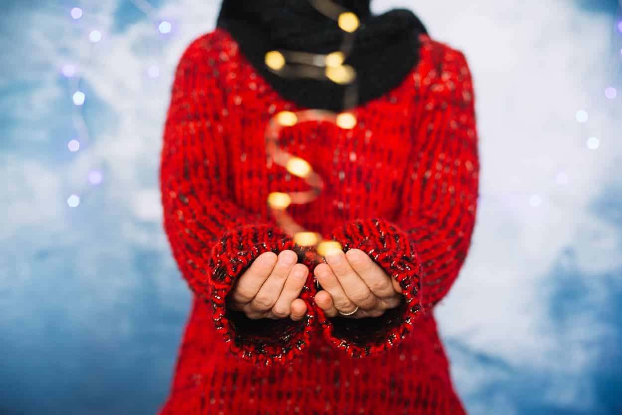 Person in red sweater holding festive string lights