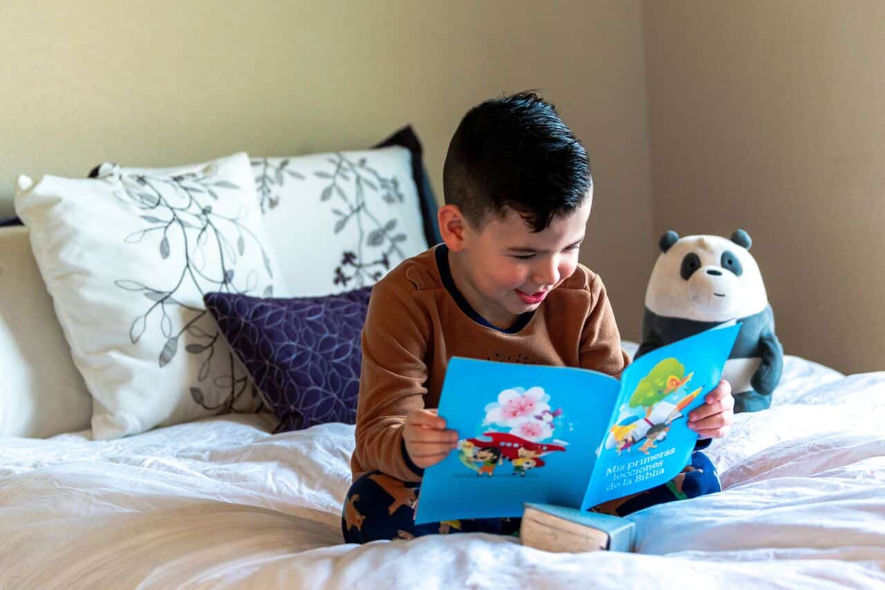 Smiling boy reading a colorful book on bed