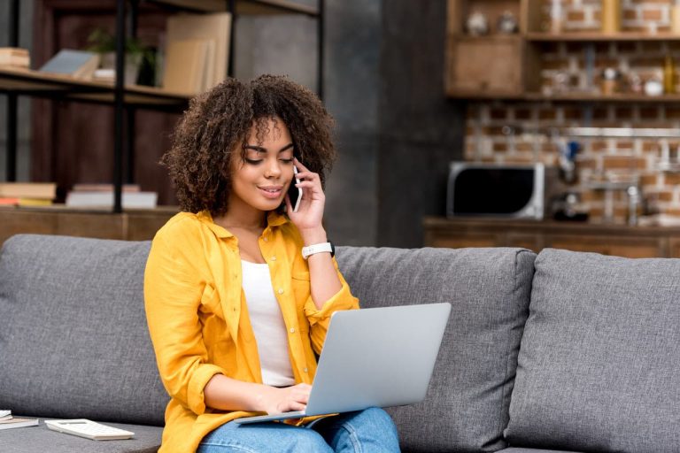 Woman sitting on a couch, using laptop while on phone