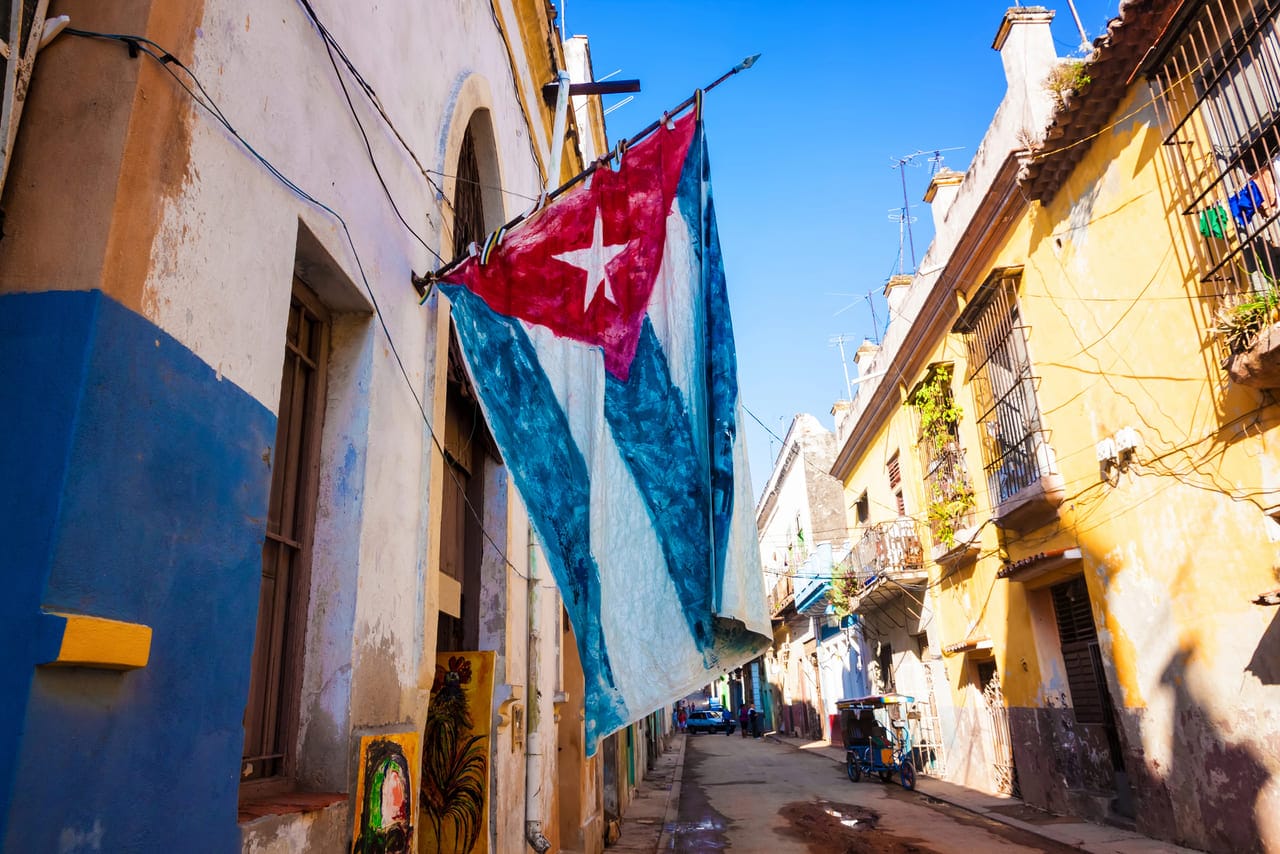 A weathered Cuban flag hanging on a narrow street.